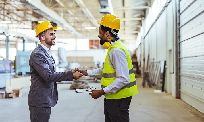 Meeting between a man in a suit and a man in high visibility gear in an Industrial Warehouse.