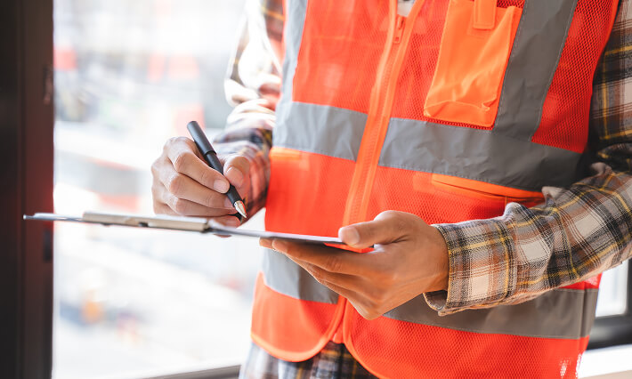 Field inspector in safety vest noting building issues on tablet in Dallas