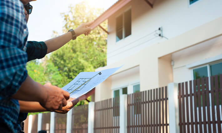 Contractors examine the outside of a residential building.