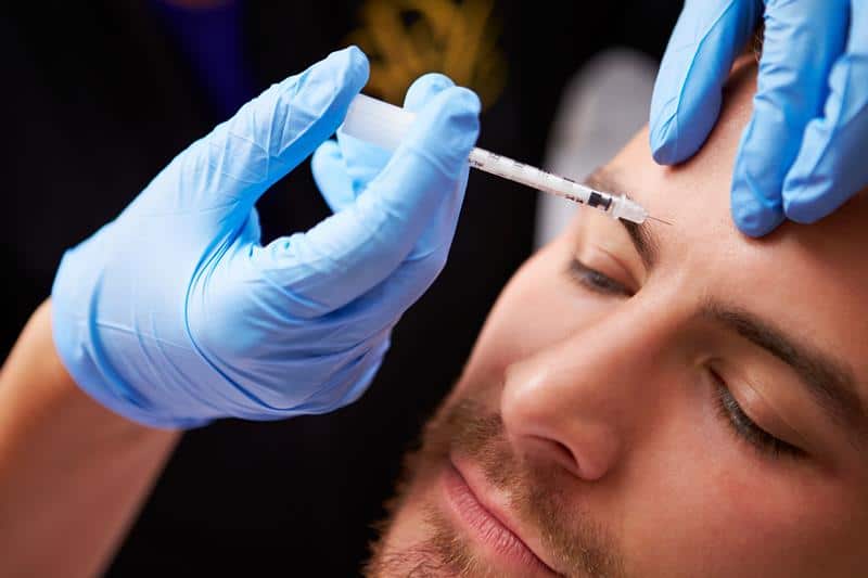 Close-up of a man receiving a Botox injection on his forehead by a medical professional.