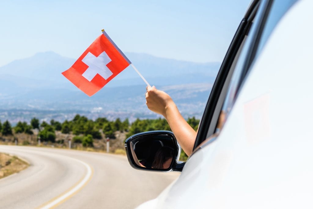 Person fährt mit dem Auto und hält eine Schweizer Flagge aus dem Fenster
