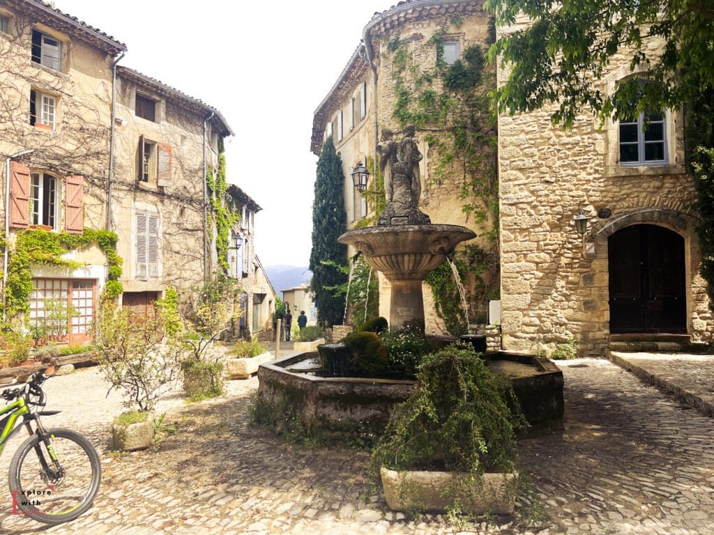 Peaceful square in Saignon, one of the best villages to see in Provence, featuring a moss-covered fountain, cobbled streets, and ivy-draped stone buildings—perfect for a quiet escape on a day trip from Aix en Provence.