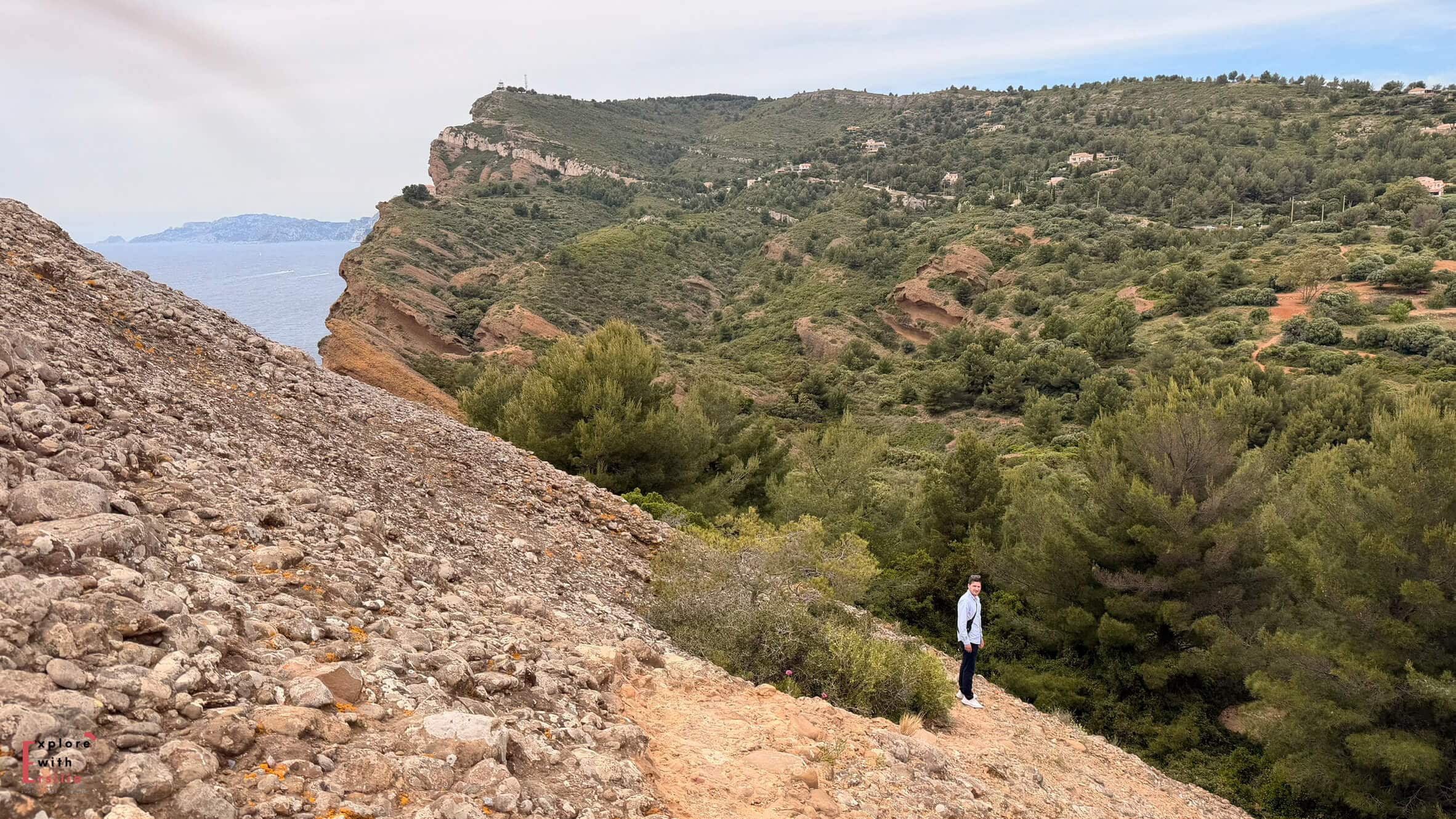 Lone hiker walking across a rocky hillside trail with sweeping views of the countryside around La Ciotat.