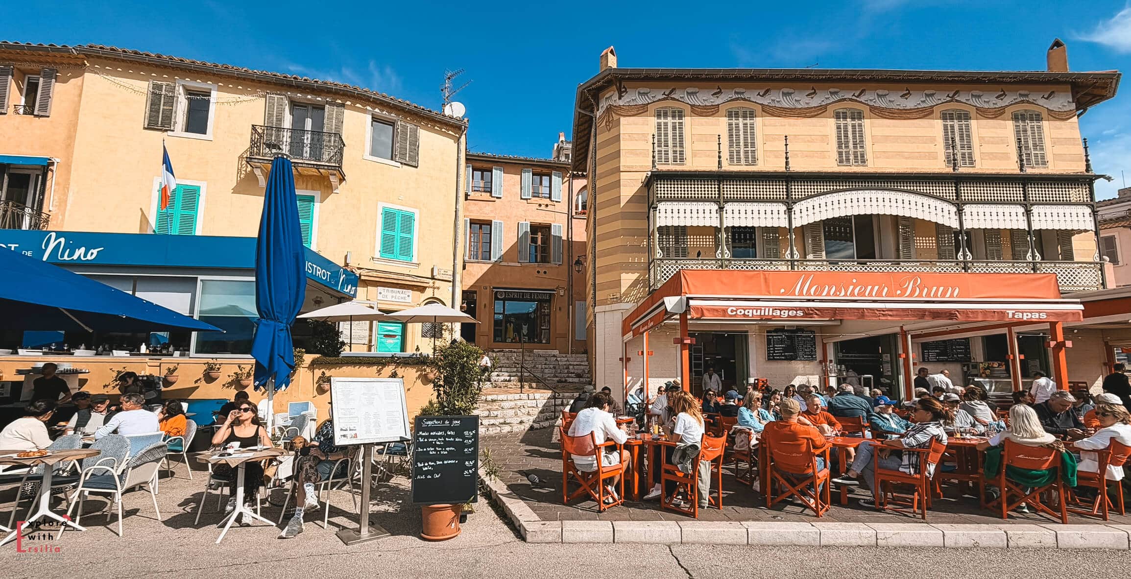 Outdoor cafés and restaurants lining the busy port of Cassis with waterfront seating overlooking the harbor.