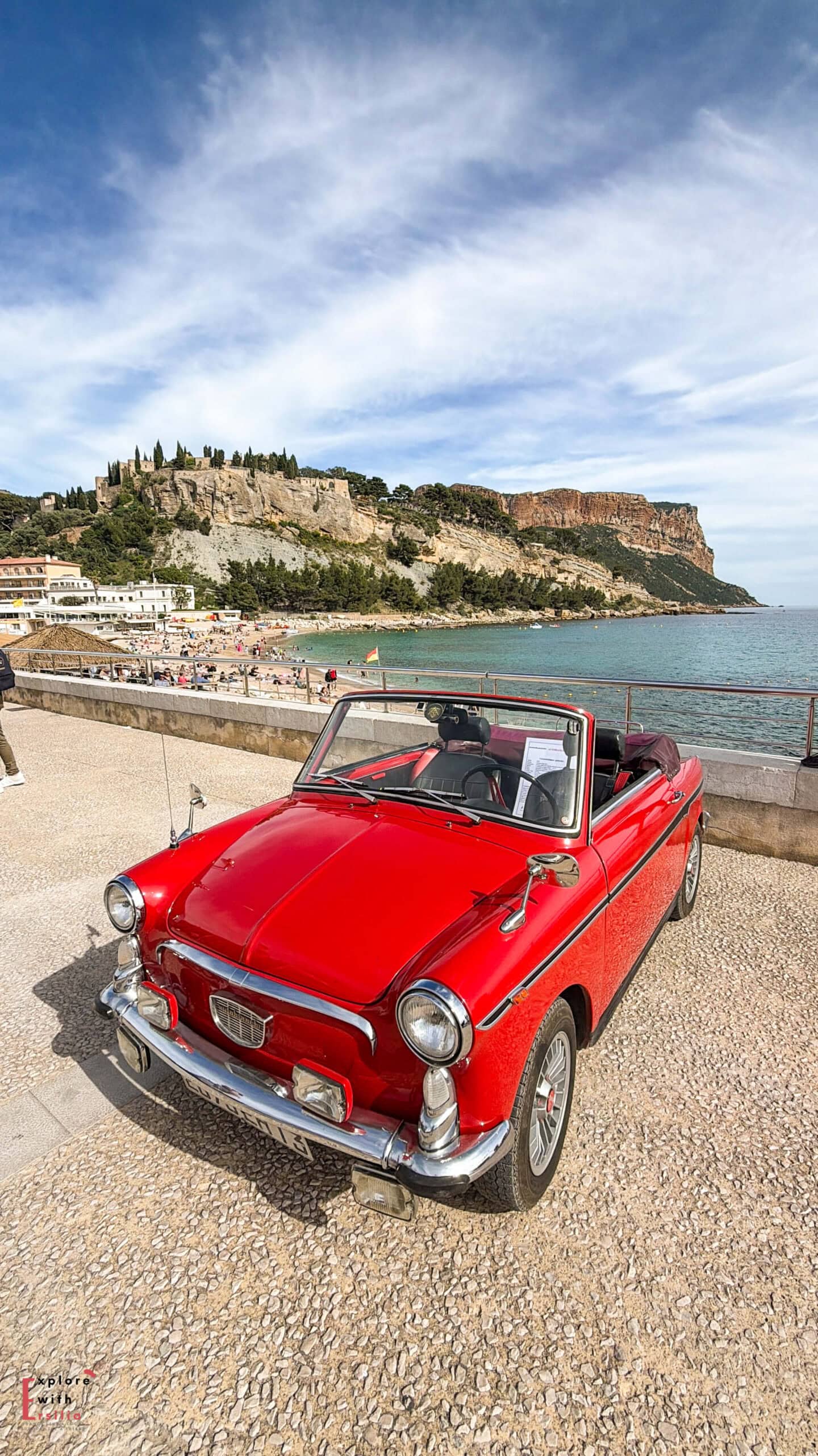 a red vintage car in front of the beach of cassis