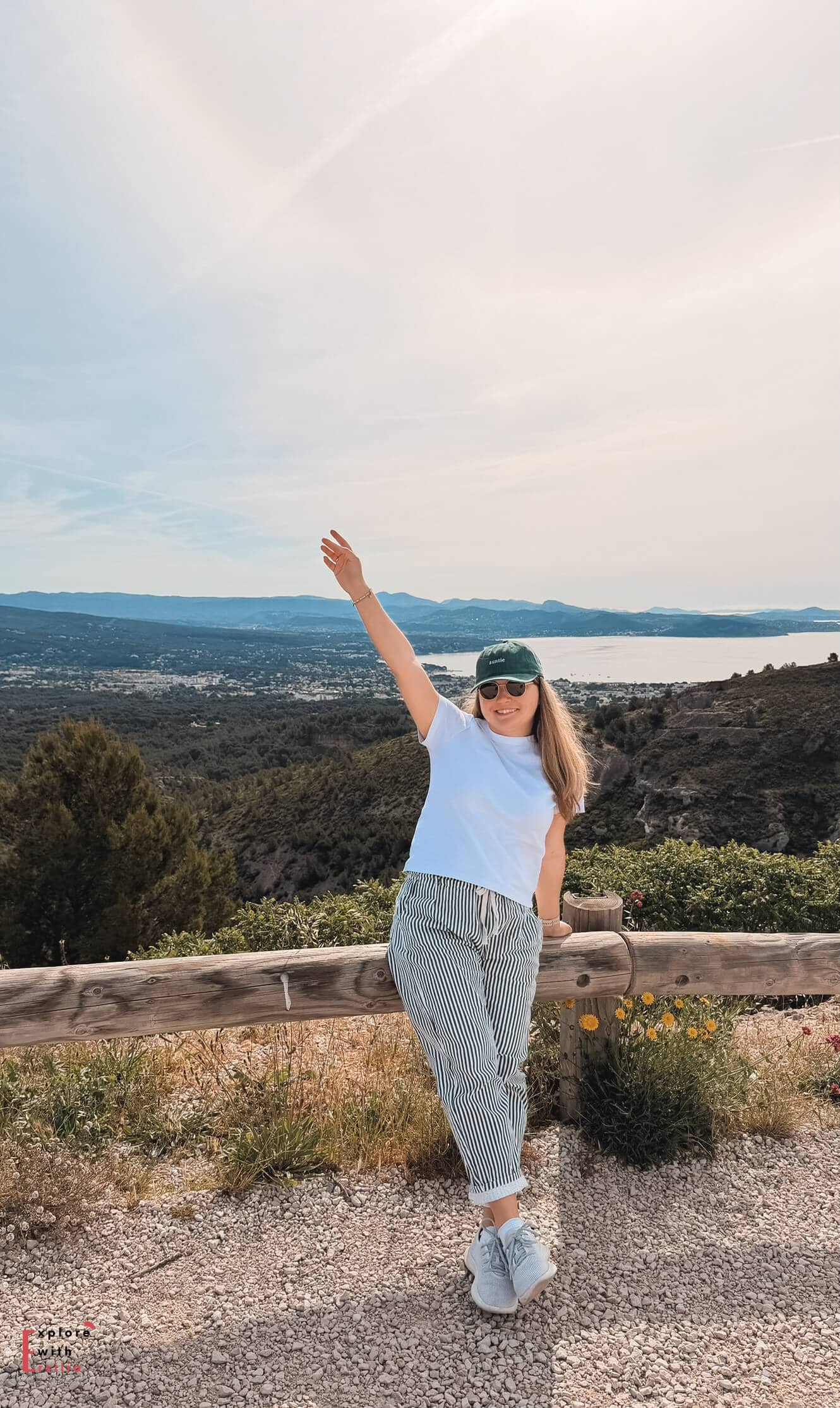 Woman posing at a Route des Crêtes viewpoint overlooking coastal cliffs, forests, and the Mediterranean coastline.