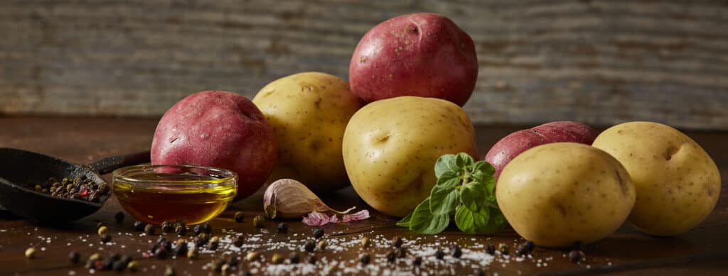 Yellow and red raw potatoes with oil, salt and pepper in rustic setting.