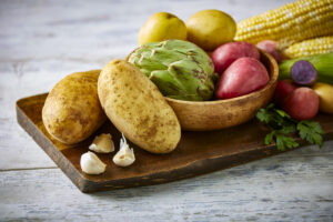 Raw russet potatoes with variety of other raw vegetables on a cutting board.
