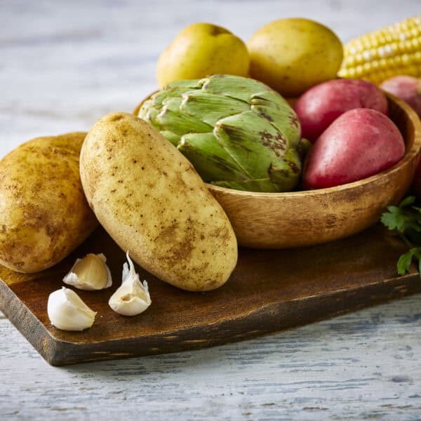 Raw russet potatoes with variety of other raw vegetables on a cutting board.