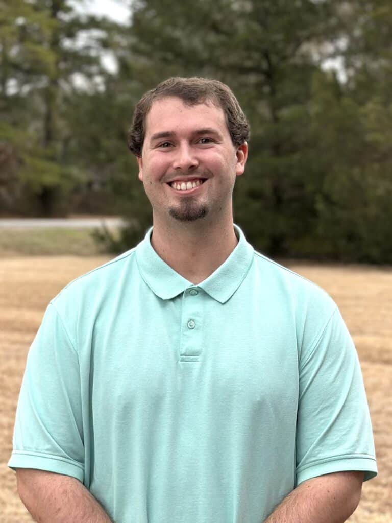 Profile of Tyler Norris in front of a row of pine trees.