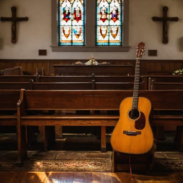 Guitar leaning against pew inside a church with stained glass windows and wooden crosses.