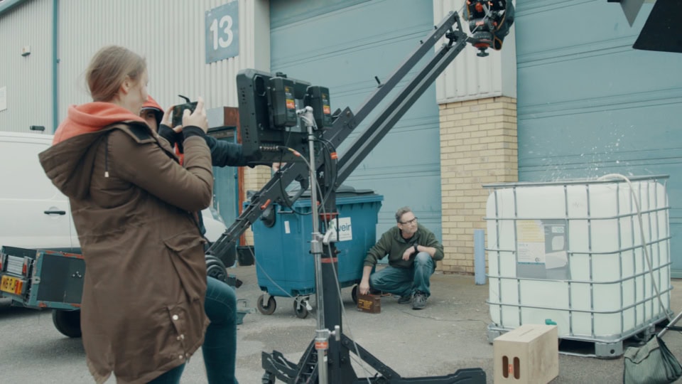 Cinematic filming scene with crew and camera equipment outside industrial warehouse.