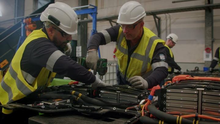Electric vehicle battery assembly in a factory, with workers in safety gear.