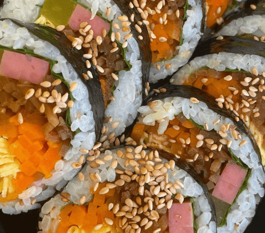 Healthy Korean vegetable Kimbap sprinkled with toasted sesame seeds, showing a vibrant cross-section.
