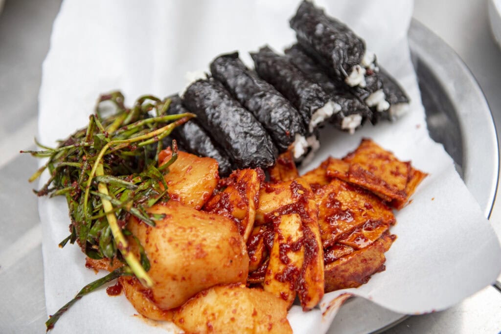 Chungmu-gimbap: Bite-sized plain seaweed rice rolls served with spicy seasoned squid and radish kimchi.
