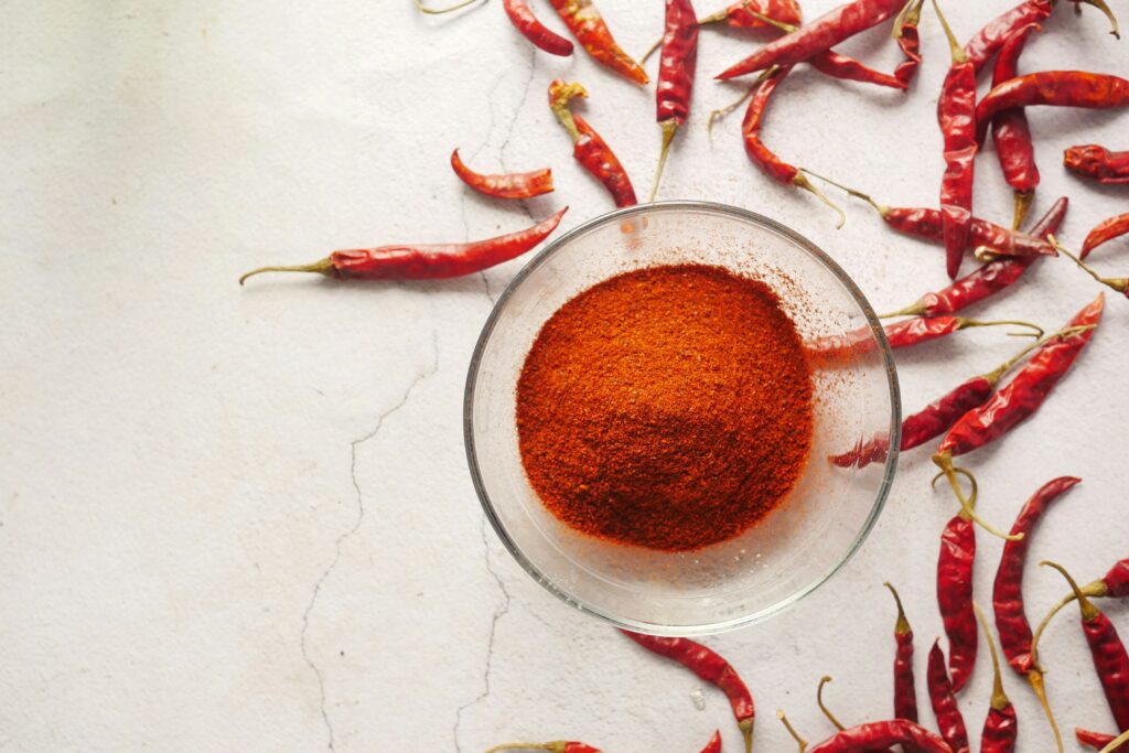 Vibrant red Korean chili powder (Gochugaru) in a traditional earthen bowl with sun-dried chilies.