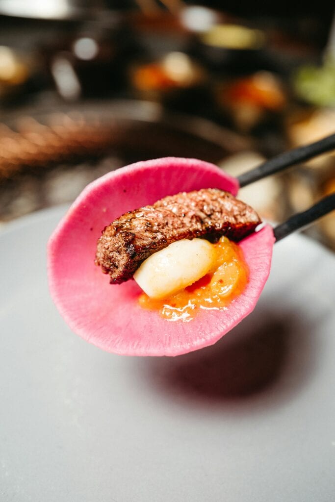 Savory grilled meat, toasted garlic, and ssamjang topped on a slice of refreshing Korean pickled radish (Ssammu).