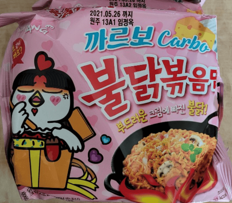Shelves of a supermarket stocked with the soft pink packaging of Samyang Carbo Buldak Bokkeum Myeon (Creamy Carbonara Spicy Chicken Ramen).