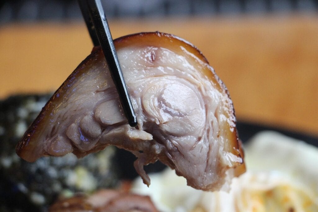 Someone holding a piece of glistening Korean Jokbal with chopsticks over a platter.