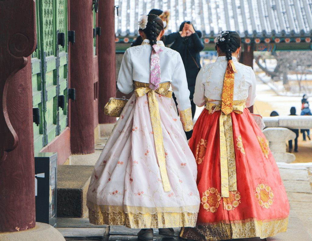 Woman in traditional Korean dress (Hanbok) walking through a Gyeongbokgung Palace courtyard, back view. Essential Hanbok experience for Seoul travel.