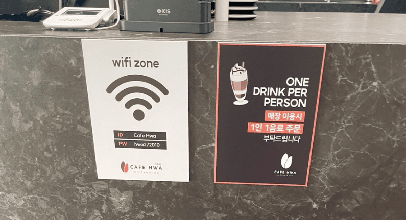 A sign in a Korean cafe displaying free Wi-Fi network names and passwords for customers.
Cafe signage stating the 'One drink per person' policy (1인 1음료) in both Korean and English.
