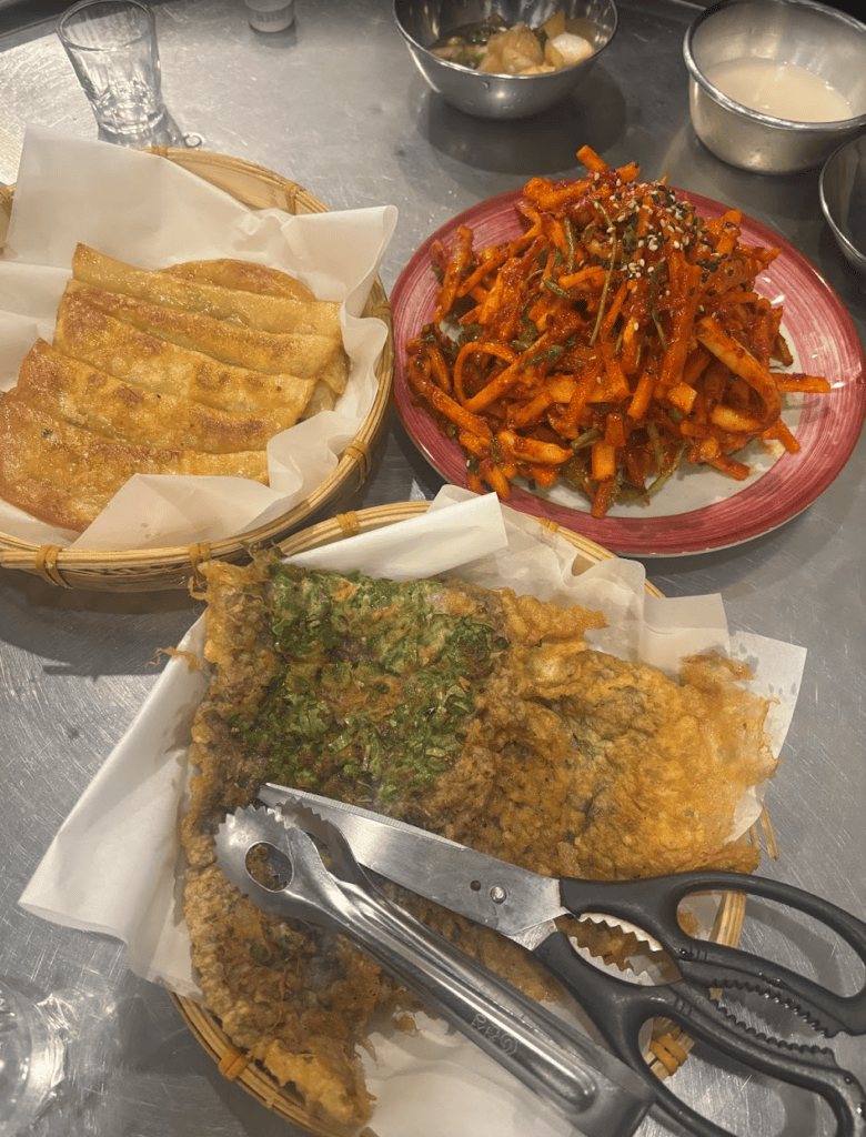 A perfect Korean 'Anju' spread featuring savory beef pancakes (Yukjeon), crispy Daegu-style flat dumplings, and a tangy spicy squid salad.