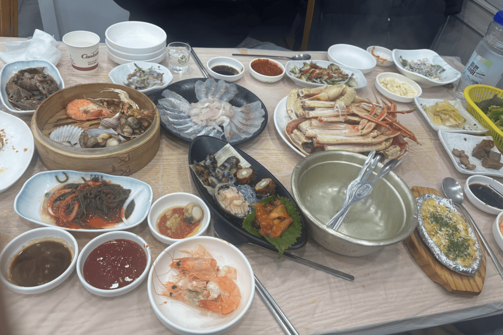 A luxurious and full Korean 'Anju' (drinking food) feast featuring a large steamed snow crab (Daege-jjim), assorted fresh sashimi (Hoe), and a variety of seafood side dishes.