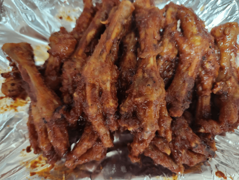 Fiery red and glossy Korean spicy Dakbal (chicken feet) served hot on a disposable silver foil plate.