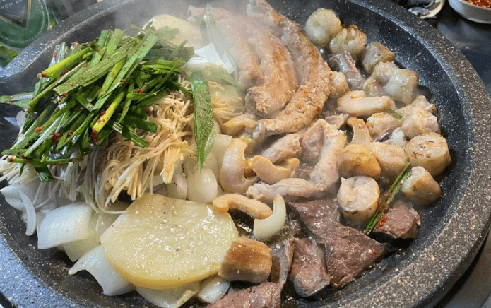 Grilled Korean beef intestines (Gopchang and Daechang) with vegetables on a hot stone grill.