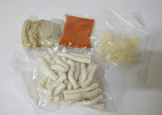 Contents of a Tteokbokki meal kit, showing individually packaged ingredients: chewy rice cakes, sliced fish cakes, a pack of spicy sauce, and fresh mixed vegetables.