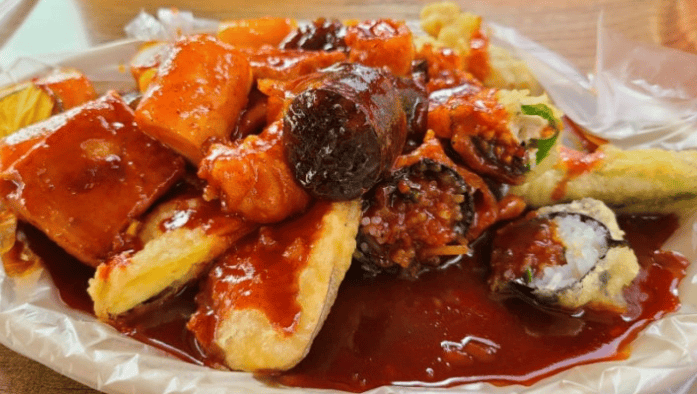 Mouth-watering "Beombeok" style Korean street food, featuring pieces of savory Sundae and crispy fried dumplings tossed in a vibrant red chili sauce.