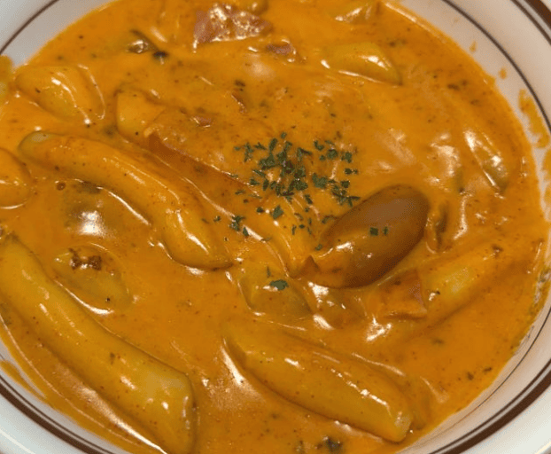 A close-up of Rosé Tteokbokki (Korean rice cakes) coated in a smooth, creamy, and vibrant orange sauce.