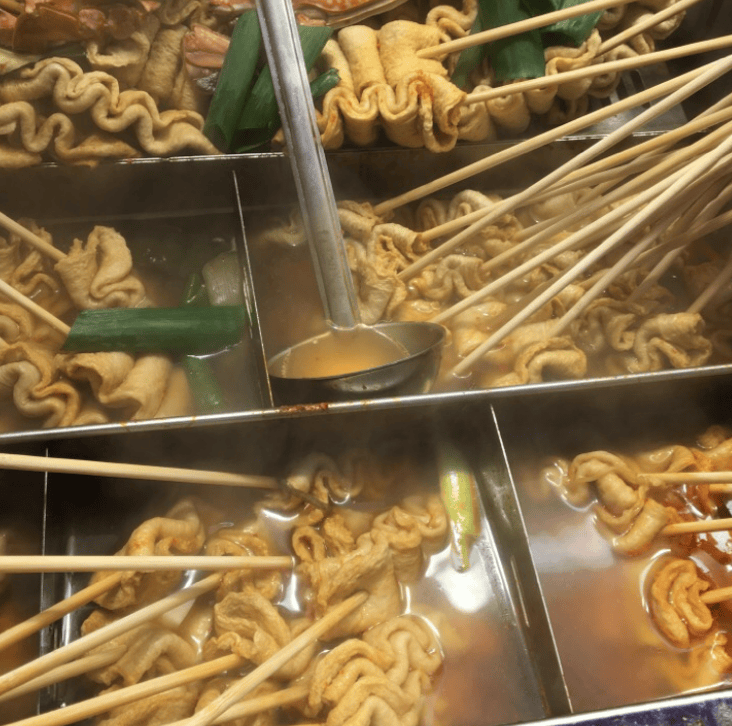 Mouth-watering Korean fish cake skewers (Eomuk-kkochi) arranged neatly in a big simmering pot at a bustling outdoor market.