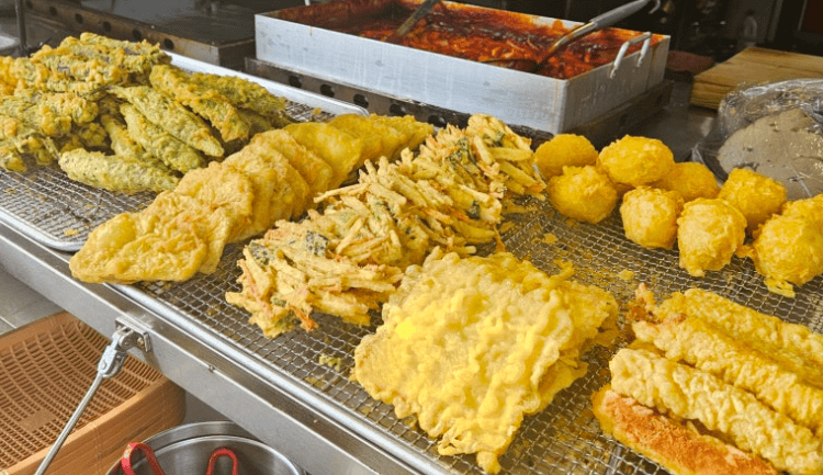 Assorted crispy Korean deep-fried snacks including sweet potato, squid, and vegetables, perfect with Tteokbokki sauce
