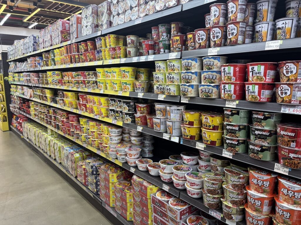Shelves at a Korean supermarket packed with a massive variety of colorful cup noodles (Cup Ramyun) in different sizes.