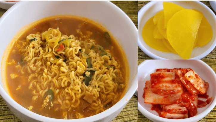 A steaming bowl of freshly cooked ramyun served with side dishes of yellow pickled radish and napa cabbage kimchi at Kimbap Cheonguk.