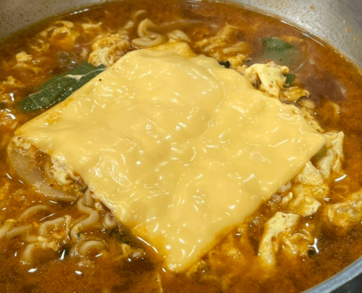 Spicy Korean ramyun topped with a slice of yellow cheddar cheese melting into the hot red broth.