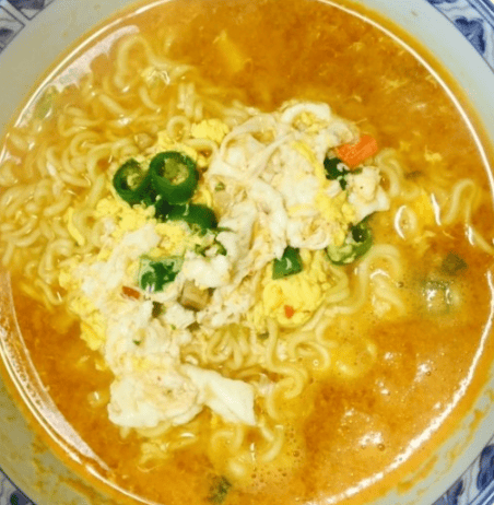 Spicy Korean ramyun in a hot red broth topped with a soft-boiled egg and green onions.