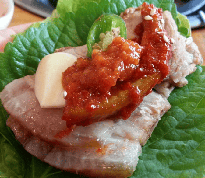 outh-watering Korean Bossam wrap in a crisp lettuce leaf, featuring layers of tender pork belly, spicy kimchi, and traditional condiments.