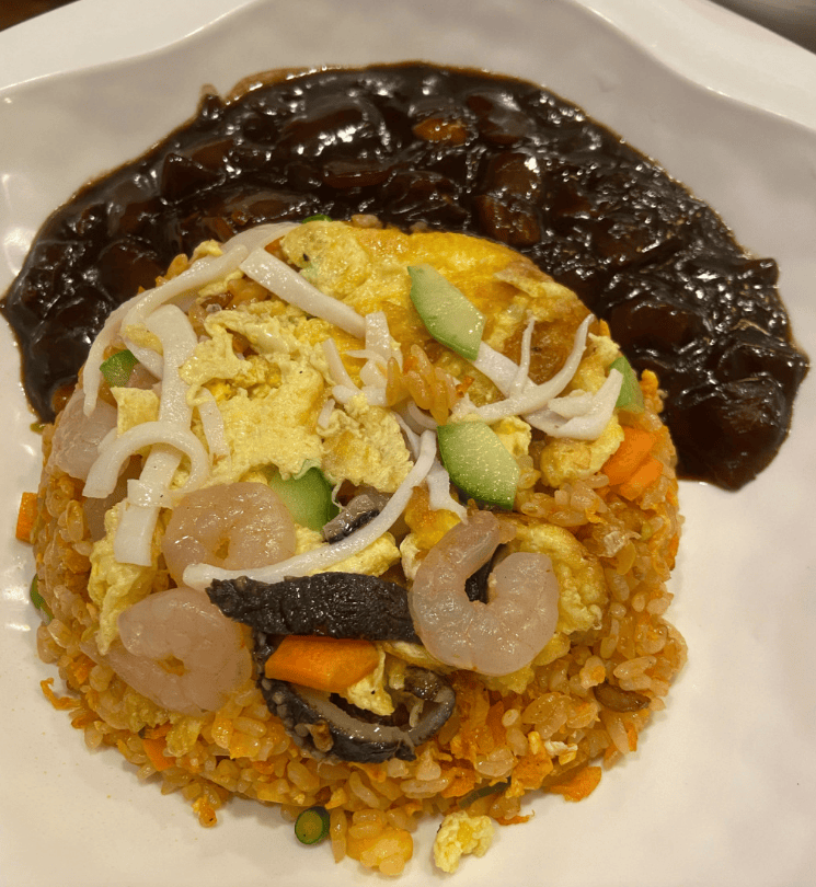 Close-up of smoky, golden-brown fried rice packed with shrimp and vegetables, accompanied by a thick, glossy Jajang sauce for a rich flavor combination.
