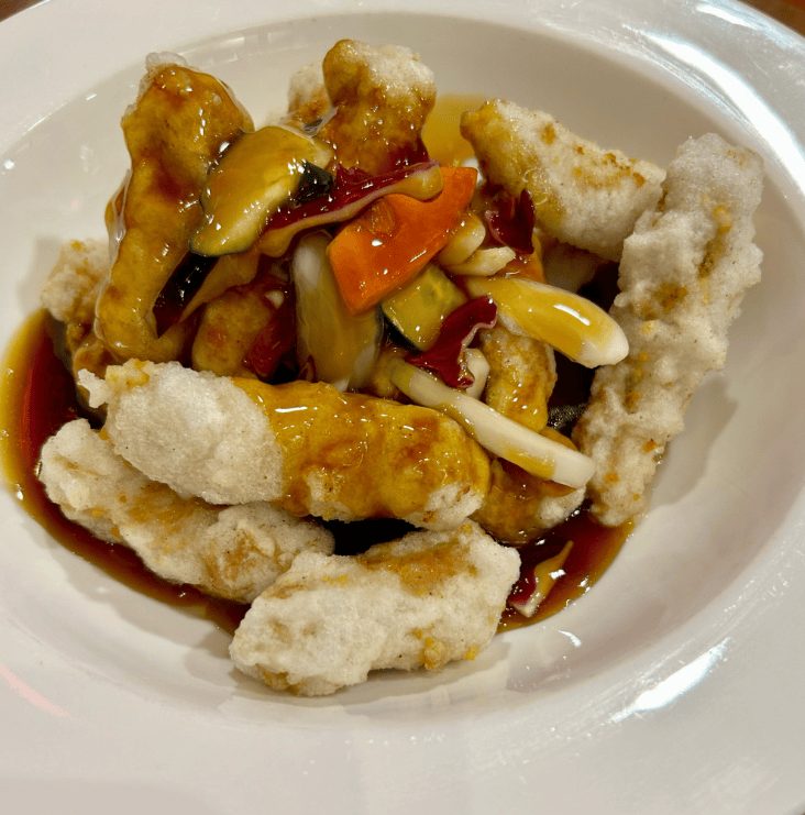 A plate of "Bumuk" style Tangsuyuk, where the glossy sweet and sour sauce is poured directly over the crispy fried pork, allowing the batter to soak up the savory flavors.