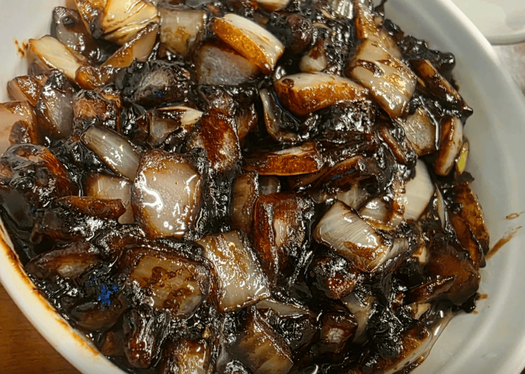 Close-up of smoky, waterless black bean sauce (Gan-jajang) with visible chunks of crunchy onions and stir-fried meat, straight from the hot wok.