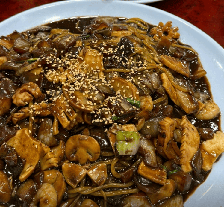 A massive platter of seafood Jaengban-jajang, featuring chewy noodles stir-fried directly with thick black bean sauce, fresh shrimp, and squid, served on a large communal tray.