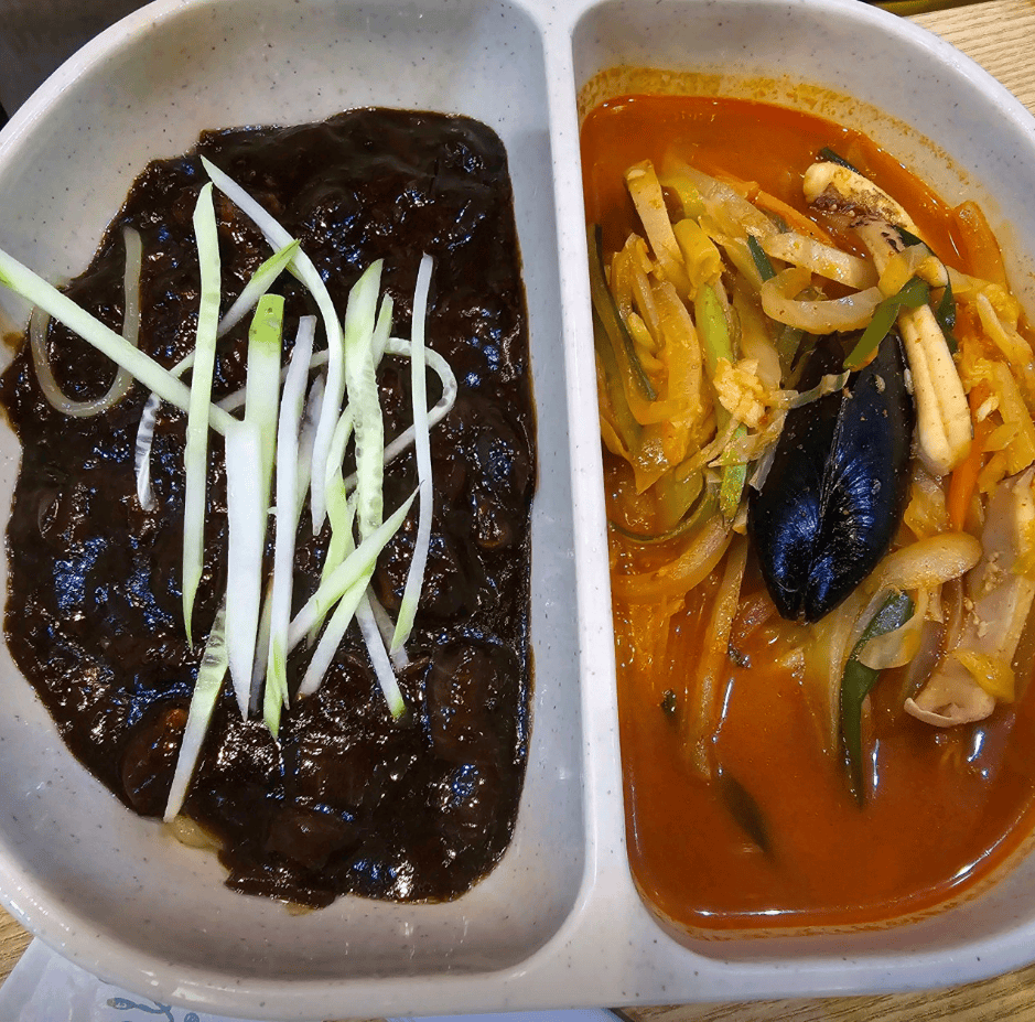 A divided bowl of Jjam-jja-myeon, featuring glossy Jajangmyeon (black bean noodles) on one side and spicy Jjamppong (seafood noodle soup) on the other, served as a perfect half-and-half meal.