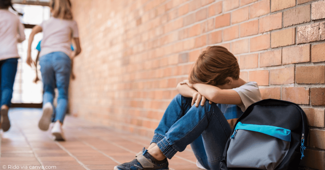 boy sitting in hallway at recess while his friends go outside to play