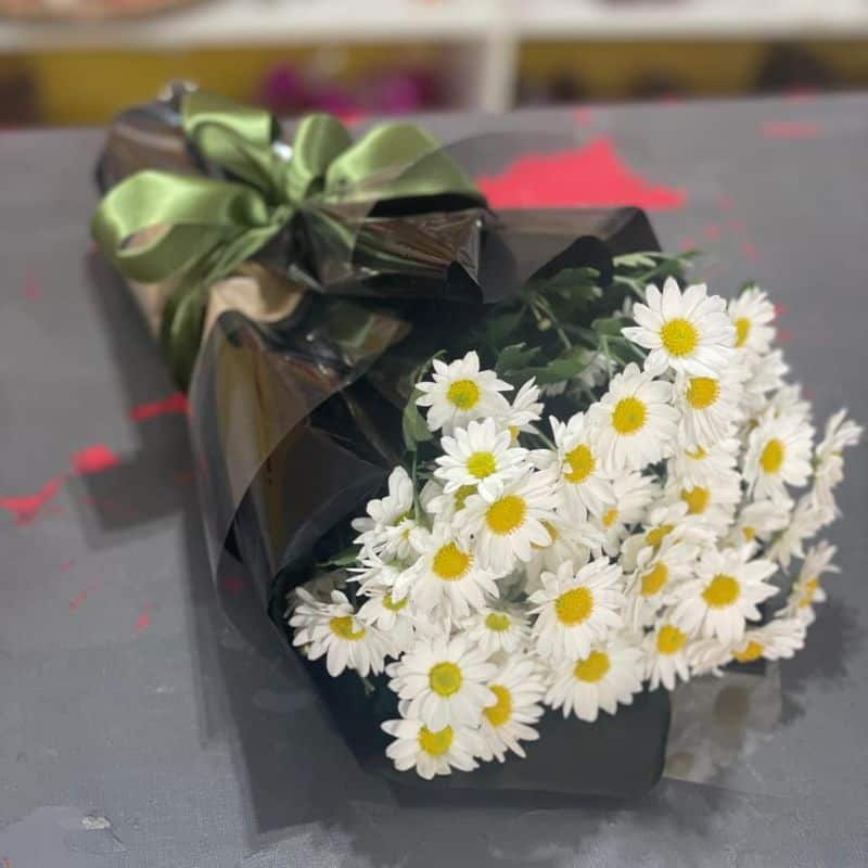 Buquê de mini margaridas brancas embalado em papel preto premium com laço verde