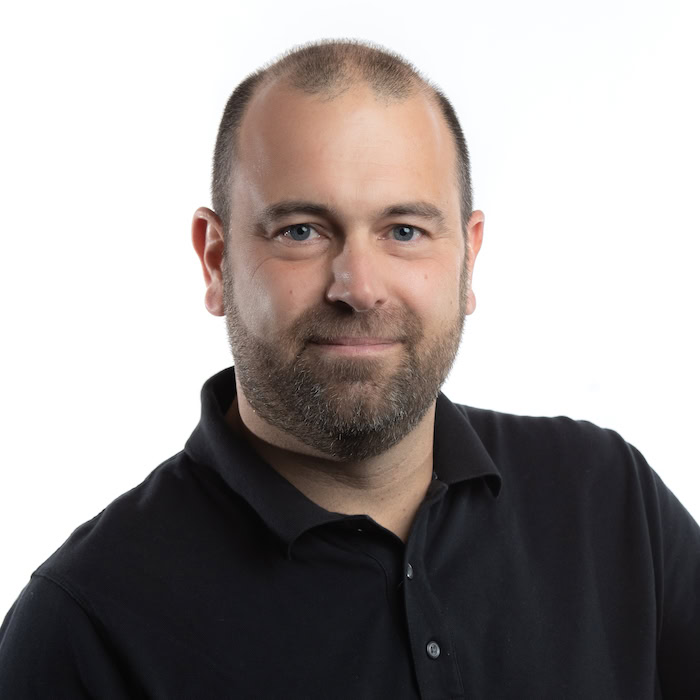Bearded man in black polo, white background, discusses LED grow lights for cannabis.
