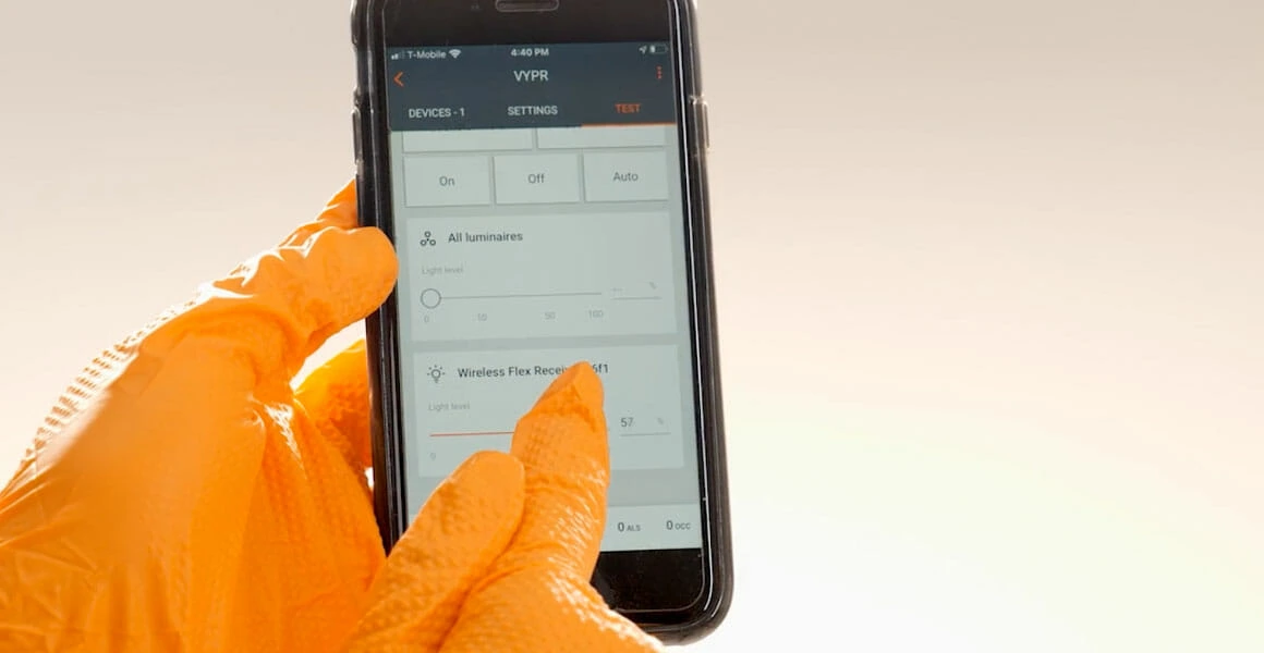 Person in orange gloves uses smartphone to control LED grow lights for cannabis.
