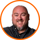 Bald bearded man smiling, wearing dark shirt, with cannabis LED grow lights.