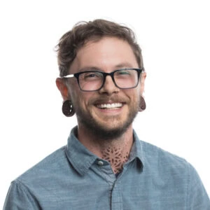 Person with glasses and tattoo poses by LED grow lights for cannabis cultivation.